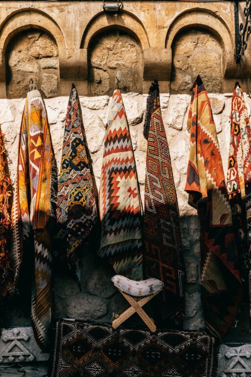 Various colorful traditional carpets with ornamental elements hanging on shabby stone wall on bazaar of ancient town on sunny street